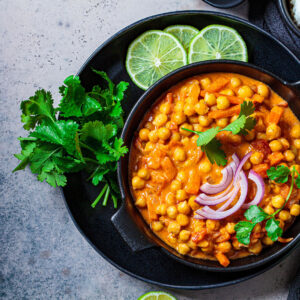 Vegan chickpea curry with rice and cilantro in a black bowl, dark background. Indian cuisine concept.